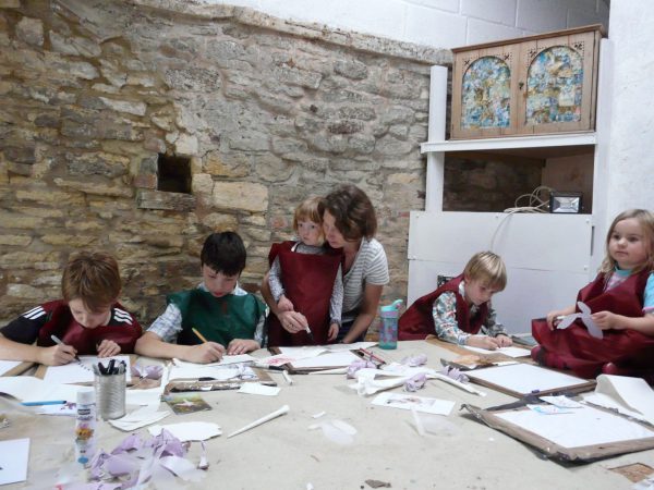 An image of a group of children of various ages and an adult. Each of them is engaged in drawing.